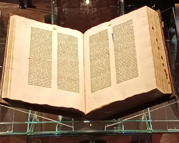 Otwarta biblia gutenberga pelplin, prezentowana na szklanym stojaku, świadectwo historii druku.