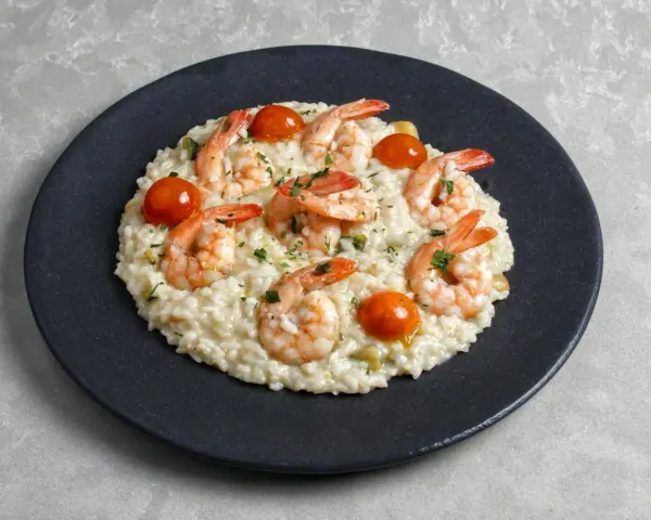 Kremowe risotto z krewetkami i pomidorkami koktajlowymi, posypane natką pietruszki. Idealny przepis na risotto dla każdego.