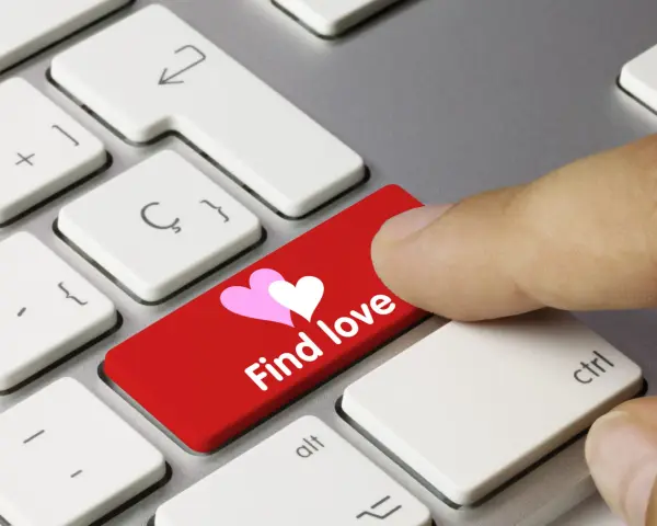 Palec naciska czerwony klawisz z sercami i napisem "Find love", symbolizując bezpieczne randki online.