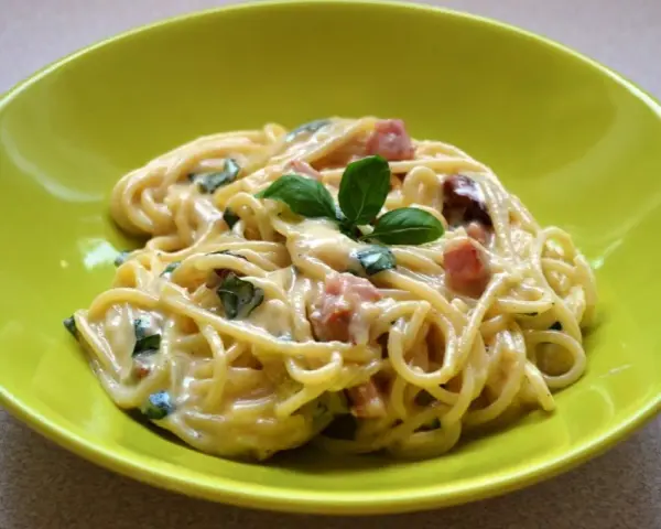 Spaghetti carbonara ze śmietaną, podane w zielonej misce, udekorowane bazylią. Pyszny przepis na klasyczne danie.