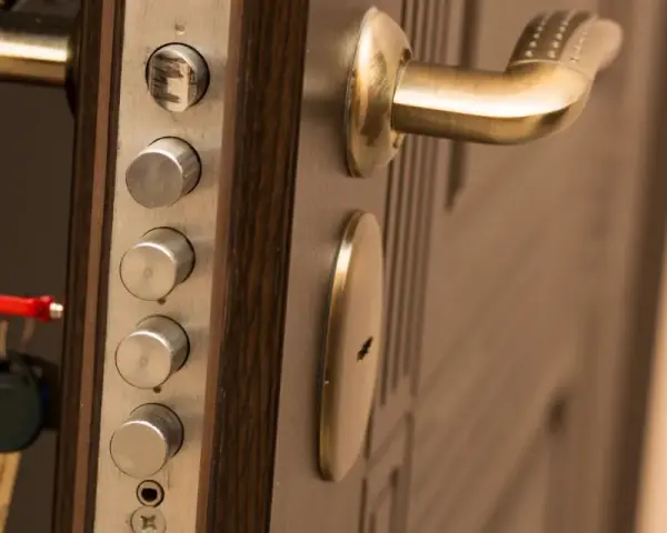 Poignée de porte blindée avec plusieurs serrures et une clé rouge. Des marques sur le cylindre supérieur suggèrent une tentative d'effraction.