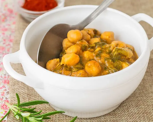 Un tazón blanco lleno de garbanzos con acelgas, un plato reconfortante y nutritivo.