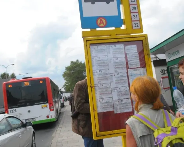Ludzie sprawdzają 79 rozkład jazdy na przystanku. Autobus linii 39 stoi obok.