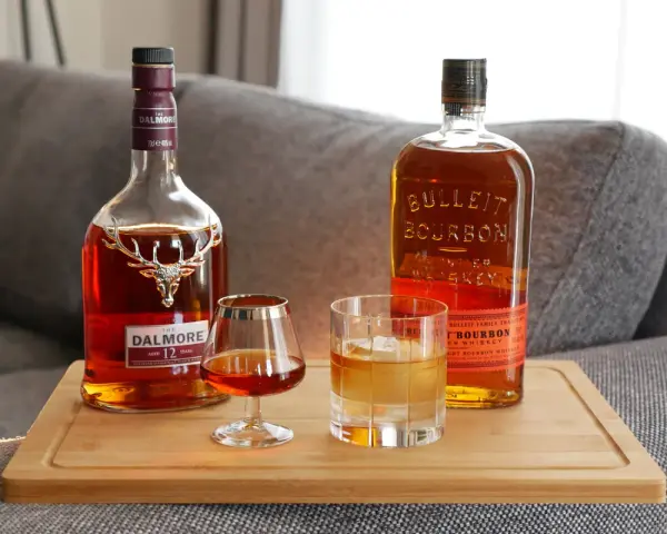 Zwei Flaschen edler Tropfen: Dalmore Scotch und Bulleit Bourbon. Ein Glas Scotch und ein Glas Bourbon mit Eis stehen bereit.
