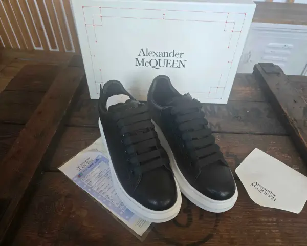 Czarne sneakersy Alexander McQueen na grubej, białej podeszwie, obok pudełka z logo marki.