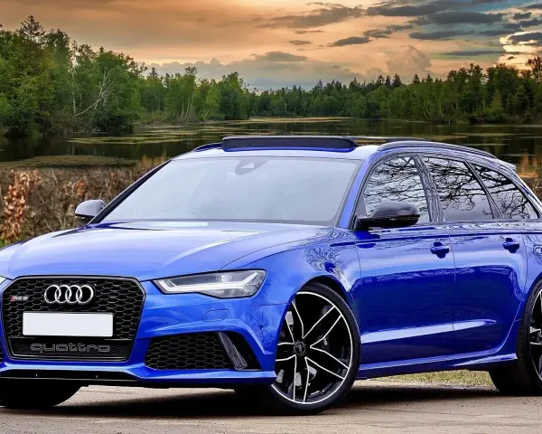 Niebieski **hatchback** z napędem quattro, zaparkowany nad jeziorem, z pięknym zachodem słońca w tle.