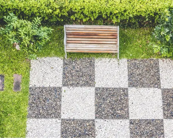 Ideas de suelo para terraza: un banco de madera sobre césped y un patrón de tablero de ajedrez de guijarros blancos y grises.