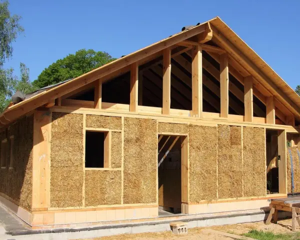 Construction d'une maison en paille écologique, avec une structure en bois visible et des murs isolés en bottes de paille.