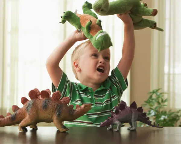 4 letnie dziecko bawi się pluszowymi dinozaurami, wyobrażając sobie prehistoryczną przygodę.