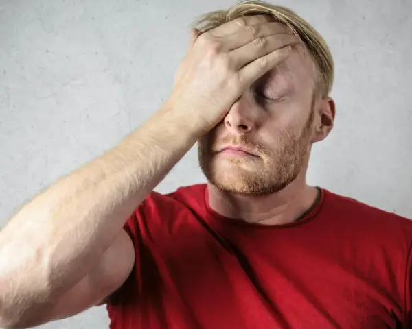 Uomo con mano sulla fronte, occhi chiusi, espressione di stress. Possibili sintomi di attacchi epilettici da stress.