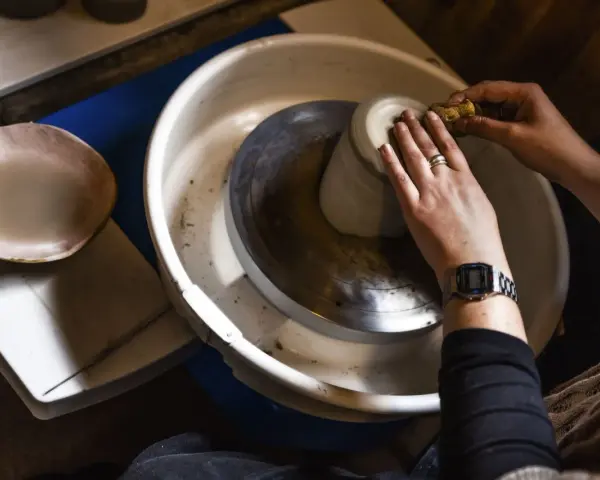 Händer som formar en mugg på en drejskiva. En svamp används för att jämna till leran medan man drejar lera.