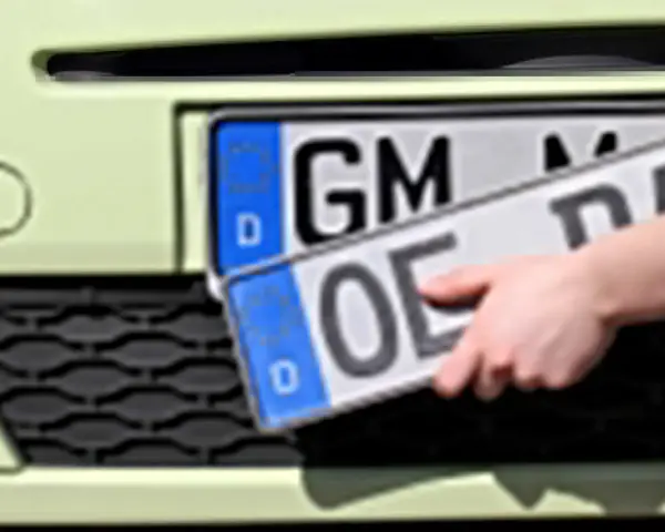 Dłoń trzyma niemieckie tablice rejestracyjne z literami "OE" i "GM".