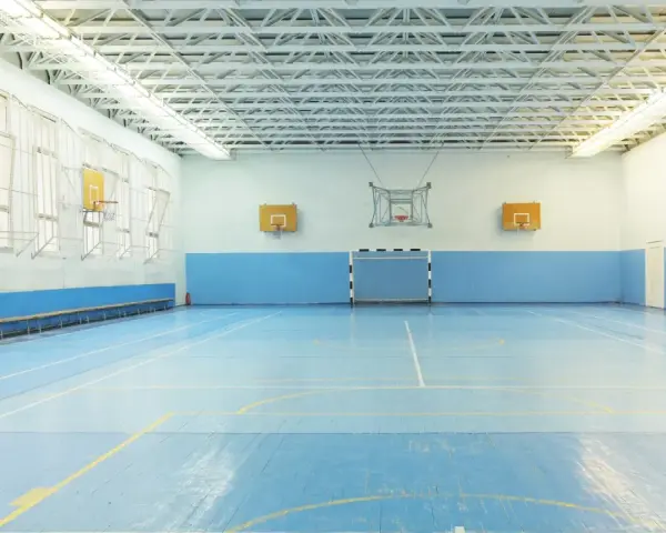 Pusta sala gimnastyczna z niebieską podłogą, boiskiem do koszykówki i piłki ręcznej. Idealne miejsce na zawody sportowe z doskonałym nagłośnieniem sali gimnastycznej.