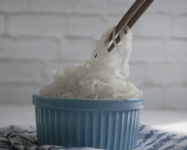 Patyczki podnoszą kłębek przezroczystego makaronu konjac z niebieskiej miseczki. To zdrowe danie, które warto wypróbować!