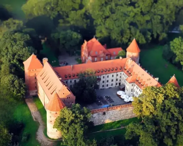 Zamek w Bytowie otoczony zielenią, z czerwonymi dachami i kamiennymi murami, wygląda jak z bajki.