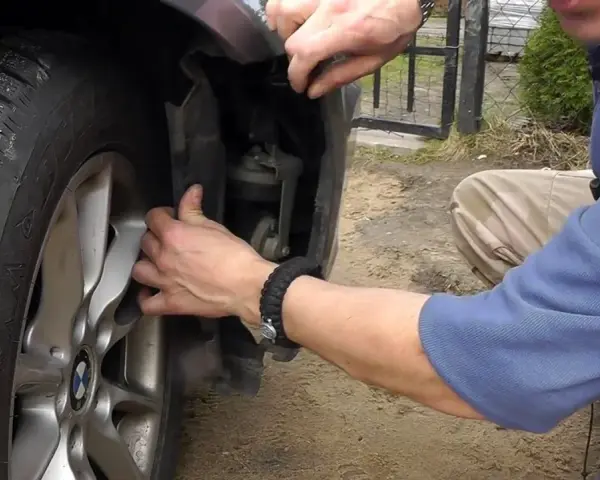 Naprawa awarii PDC BMW. Mężczyzna demontuje fragment nadkola, by dostać się do czujników parkowania.