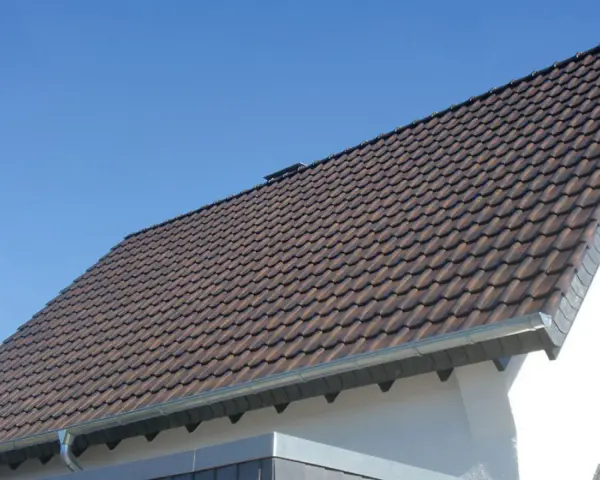 Dachówki ceramiczne na dachu domu, z widocznym okapem. Okap jest kluczowy, by wiedzieć, ile powinien wystawać dach poza ścianę, chroniąc ją przed deszczem.
