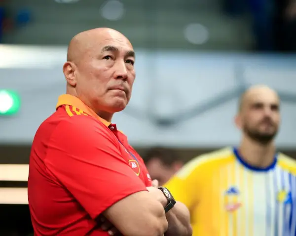 Skupiony trener Vive Kielce w czerwonej koszulce z pomarańczowym kołnierzem, z rękami skrzyżowanymi na piersi.