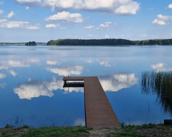 Drewniane molo na spokojnym jeziorze Wysockim, odbijającym błękitne niebo z białymi chmurami.