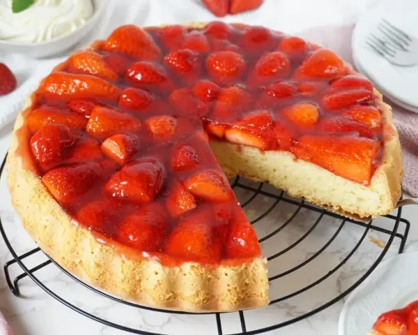 Ein saftiger tortenboden mit erdbeeren, bedeckt mit glänzendem Tortenguss. Ein Stück wurde bereits entnommen, um die köstliche Füllung zu zeigen.