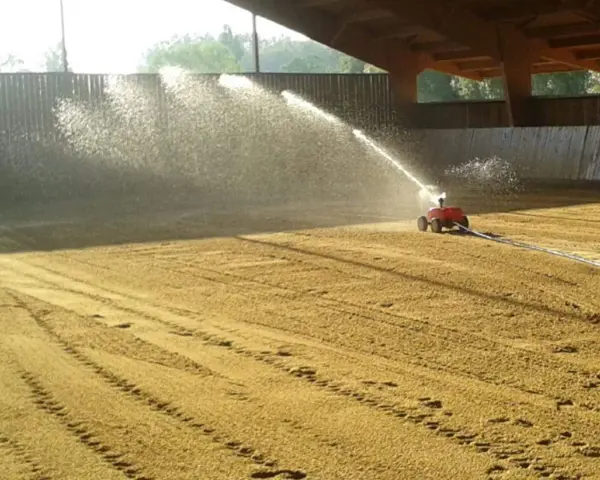 Arrosage d'une carrière équestre par un système mobile, créant un voile d'eau sur le sable.