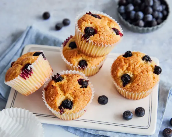 Saftige vegane Blaubeermuffins mit frischen Blaubeeren, auf einem weißen Teller mit blauer Serviette.