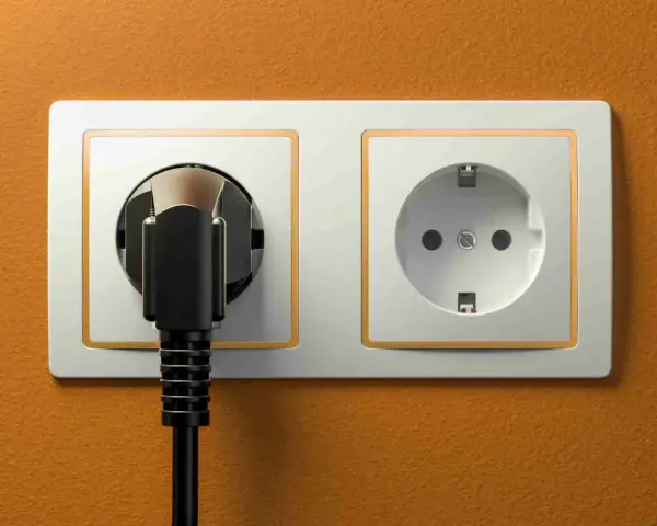 Dwa gniazdka elektryczne na pomarańczowej ścianie. Jedno z nich jest puste, drugie z wtyczką. Zastanawiasz się, jakie gniazdka w Egipcie?