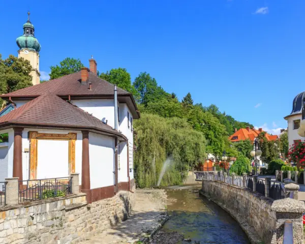 Urokliwy strumyk w Polanicy Zdrój, otoczony kamiennymi murkami i zielenią. W tle widać wieżę kościelną i kolorowe kamieniczki.