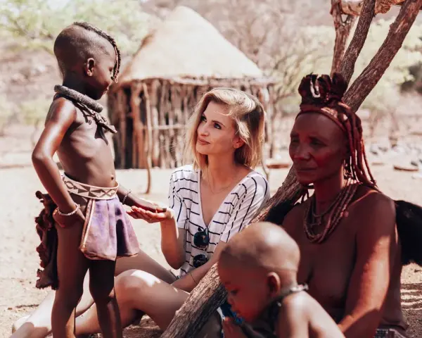 Ludzie Himba w Namibii: młoda kobieta rozmawia z dzieckiem i starszą kobietą w tradycyjnych strojach.