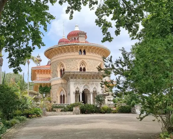 The enchanting Monserrate Palace, with its distinctive red domes and intricate stonework, is framed by lush greenery and tall trees.