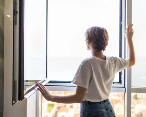 Frau stellt das Fenster ein, um frische Luft hereinzulassen.