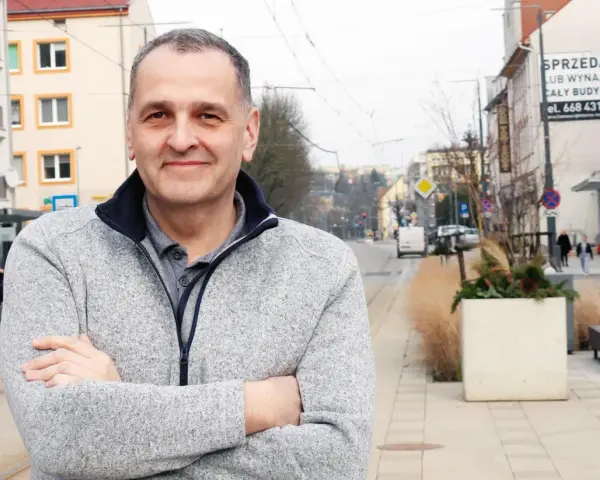 Sebastian Pieńkowski stoi na tle miejskiej ulicy z tramwajami i budynkami.
