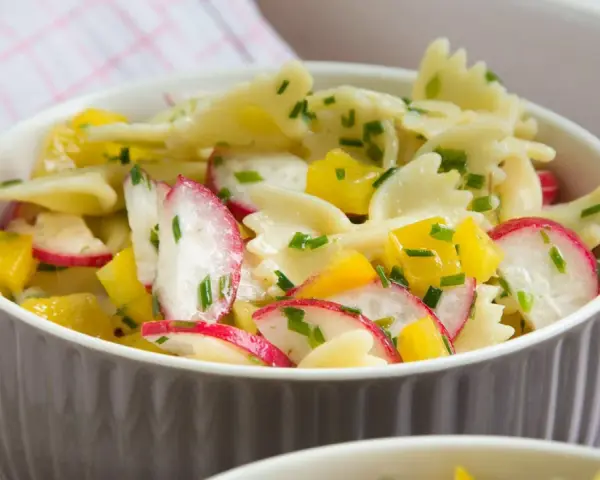 Ein bunter Nudelsalat mit Farfalle, Radieschen und gelben Paprikawürfeln, garniert mit Schnittlauch. Perfekt für den Sommer!