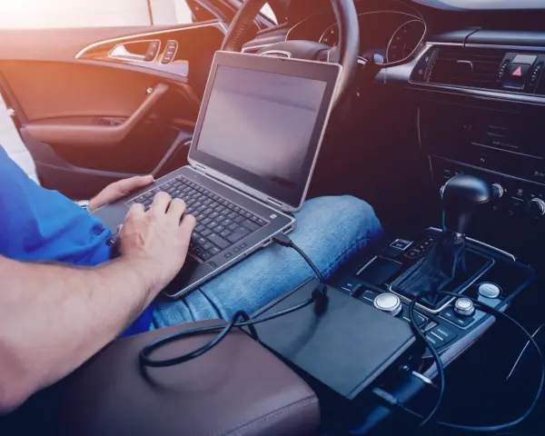 Mężczyzna w samochodzie podłącza laptopa do zasilania, pokazując, jak podłączyć komputer do samochodu.