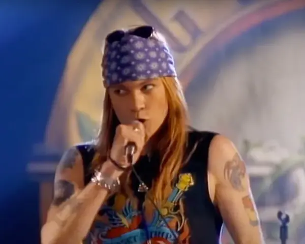 Axl Rose w fioletowej bandanie i czarnej koszulce śpiewa do mikrofonu, jakby dedykował "sweet child o' mine" publiczności.