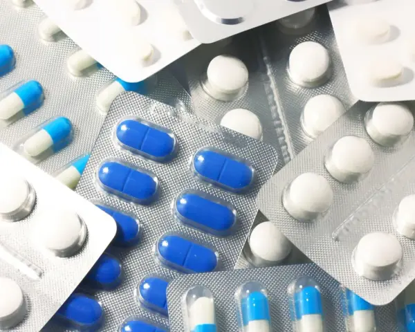 Blistry z białymi i niebiesko-białymi kapsułkami oraz białe tabletki. Wśród nich można znaleźć polopirynę, która pomaga złagodzić ból i gorączkę.