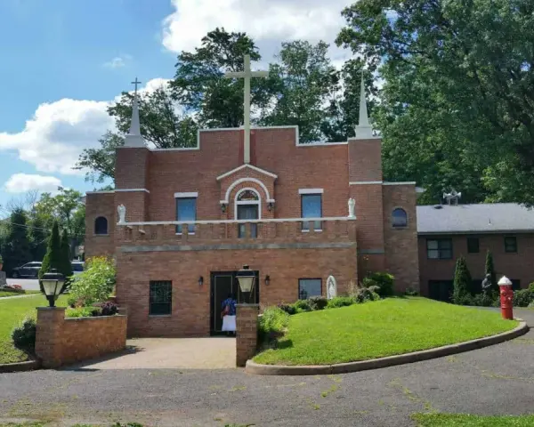 The Holy Face Monastery, a brick building with a large cross, stands on a sunny day.