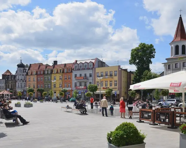 Kolorowy brodnica rynek tętni życiem. Ludzie odpoczywają na ławkach, a kawiarniany ogródek zaprasza do relaksu pod białym parasolem.