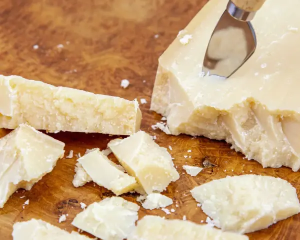 Kawałki Grana Padano na drewnianej desce, gotowe do posypania makaronu lub dodania do sosów.