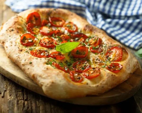 Pyszna focaccia z pomidorkami koktajlowymi i bazylią. Idealna jako dodatek do dań lub samodzielna przekąska. Z czym jeść focaccię? Z wszystkim, co lubisz!