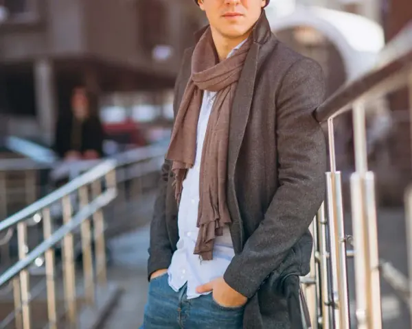 Uomo con cappotto grigio, camicia azzurra e pashmina marrone, un esempio di come indossare una pashmina in modo chic.