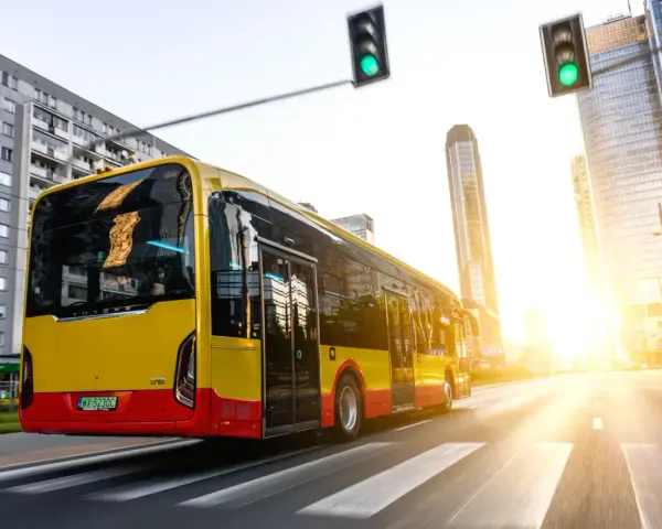 Żółto-czerwony autobus elektryczny Yutong jedzie przez miasto w blasku zachodzącego słońca.