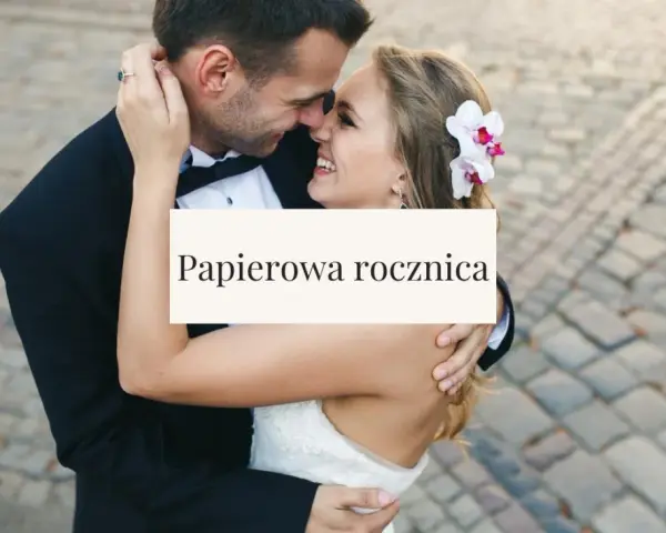 Para świętuje papierową rocznicę ślubu. Uśmiechnięci, w objęciach, z kwiatem we włosach panny młodej.