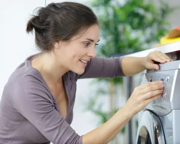 Lächelnde Frau stellt ein Programm an der Waschmaschine ein, um sie zu entkalken.