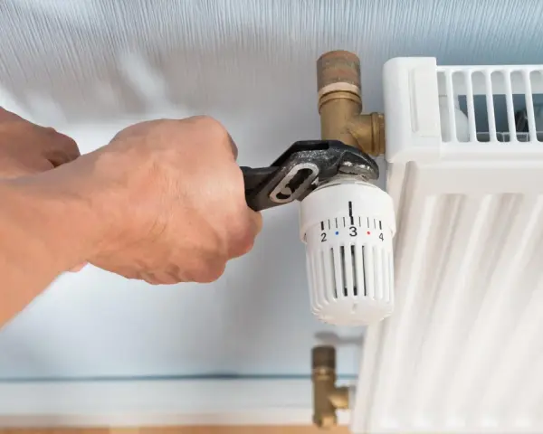Hände wechseln einen Heizkörperthermostat mit einer Rohrzange.