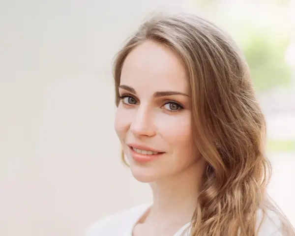 Uśmiechnięta kobieta z mysi blond włosami, delikatnie falującymi na ramionach.
