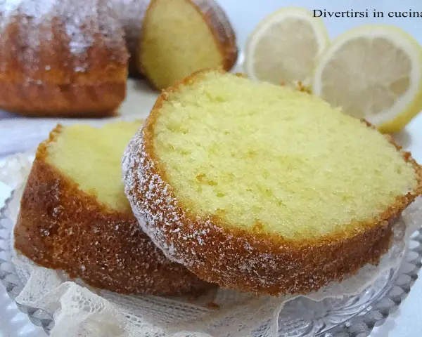 Fette di ciambellone al limone spolverate di zucchero a velo, con fette di limone sullo sfondo.
