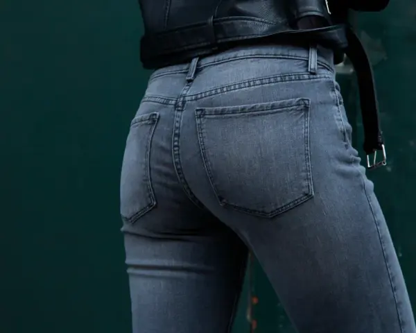 Vue arrière d'une femme portant un jean gris à coupe ajustée, avec une veste en cuir noir.