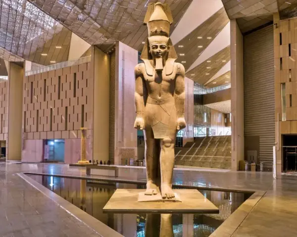 Gigantyczny posąg faraona w holu nowego muzeum w Egipcie, z nowoczesną architekturą i wodnymi elementami.
