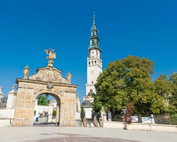 Brama na Jasną Górę, gdzie pielgrzymi zastanawiają się, ile ma lat to miejsce o bogatej historii. Wieża klasztoru góruje nad zielenią.